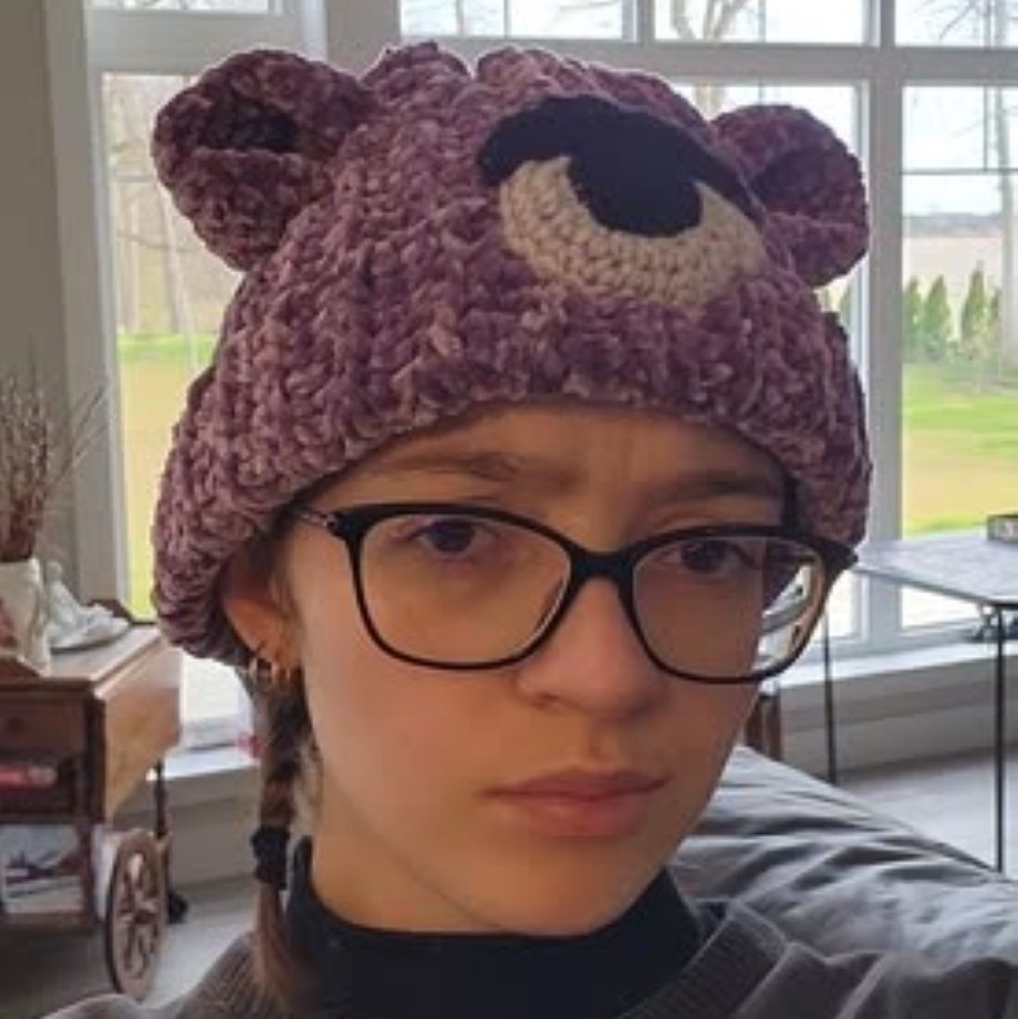 A purple crochet had with one black and grey eye and purple bear ears