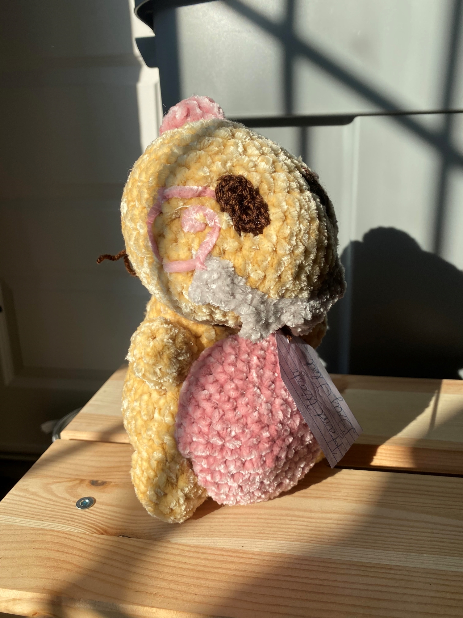 A yellow crochet dinosaur with a pink belly and spiky white teeth